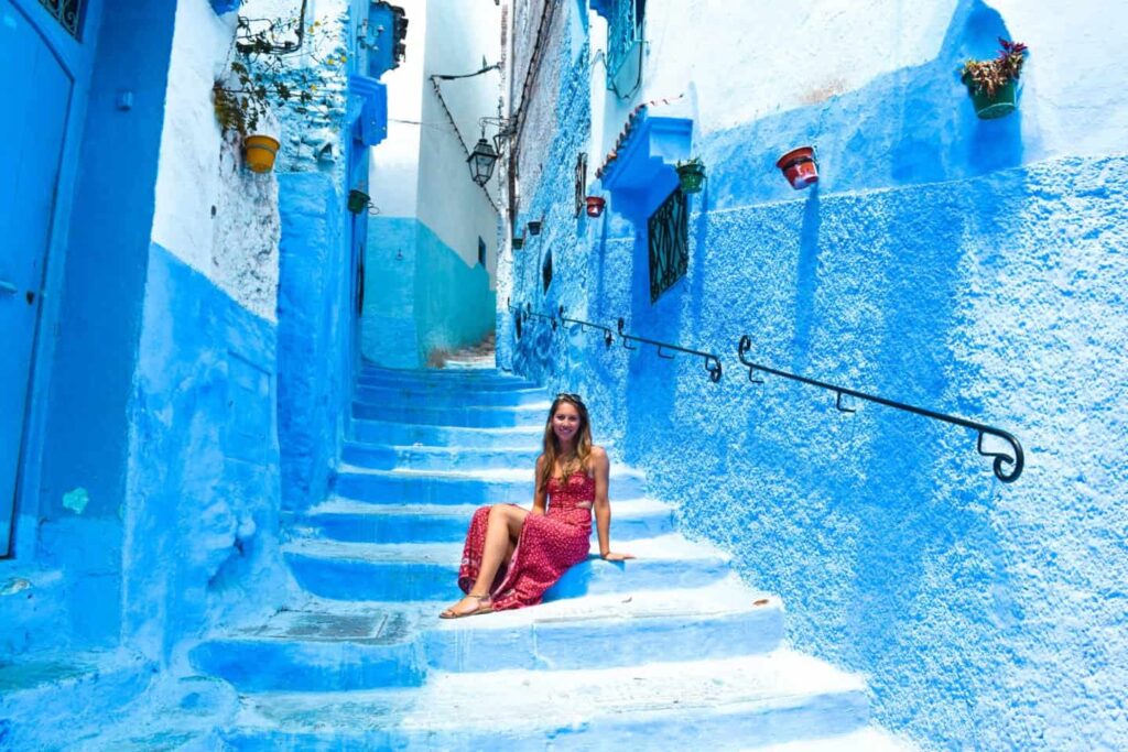 Woman in a red dress sits on a bright blue stairway in a narrow blue-painted alley.
