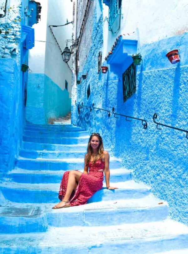 Woman in a red dress sits on a bright blue stairway in a narrow blue-painted alley.